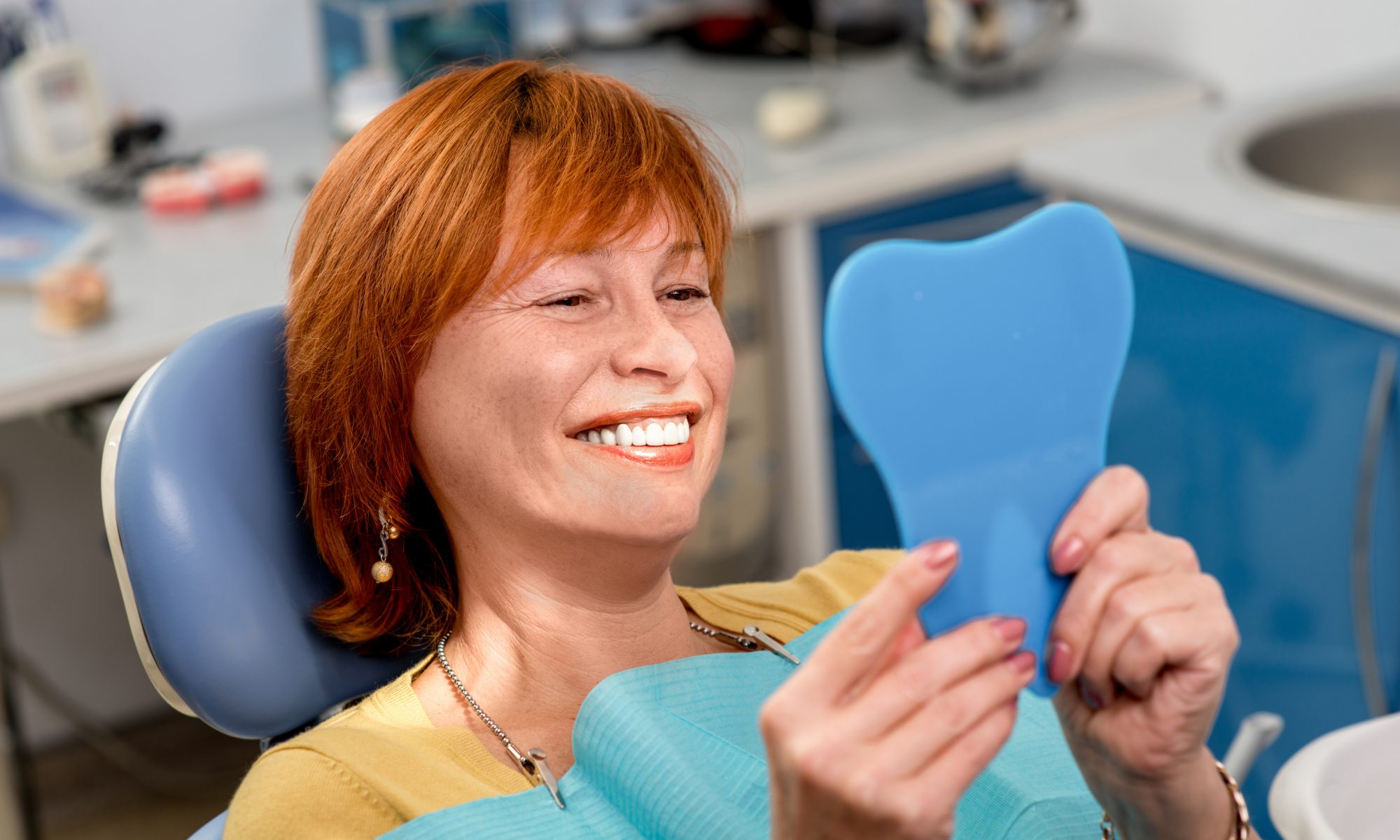 A woman smiling at her reflection because she has healthy teeth, or because she is seeing the result of dental restoration surgery