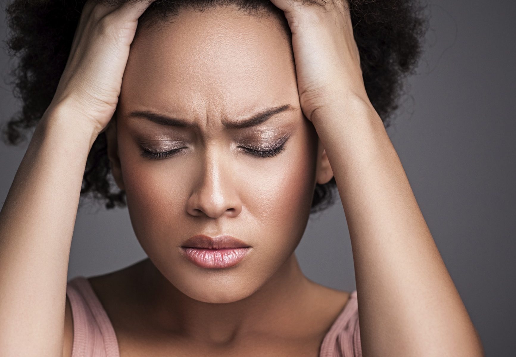 A woman holding her head in distress, likely from a toothache, or symptoms that result from poor dental hygiene